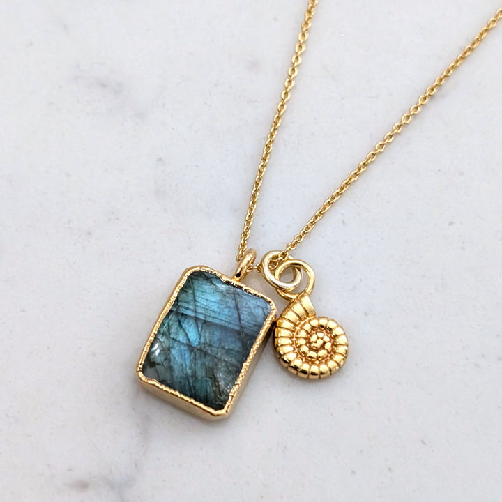 A gold-plated necklace featuring a rectangular labradorite pendant and a ammonite charm.