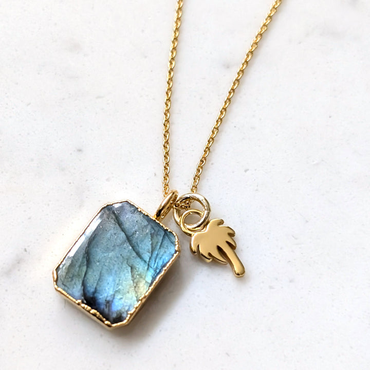 A gold-plated necklace featuring a rectangular labradorite pendant and palm tree charm.
