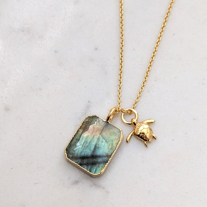 A gold-plated necklace featuring a rectangular labradorite pendant and turtle charm.