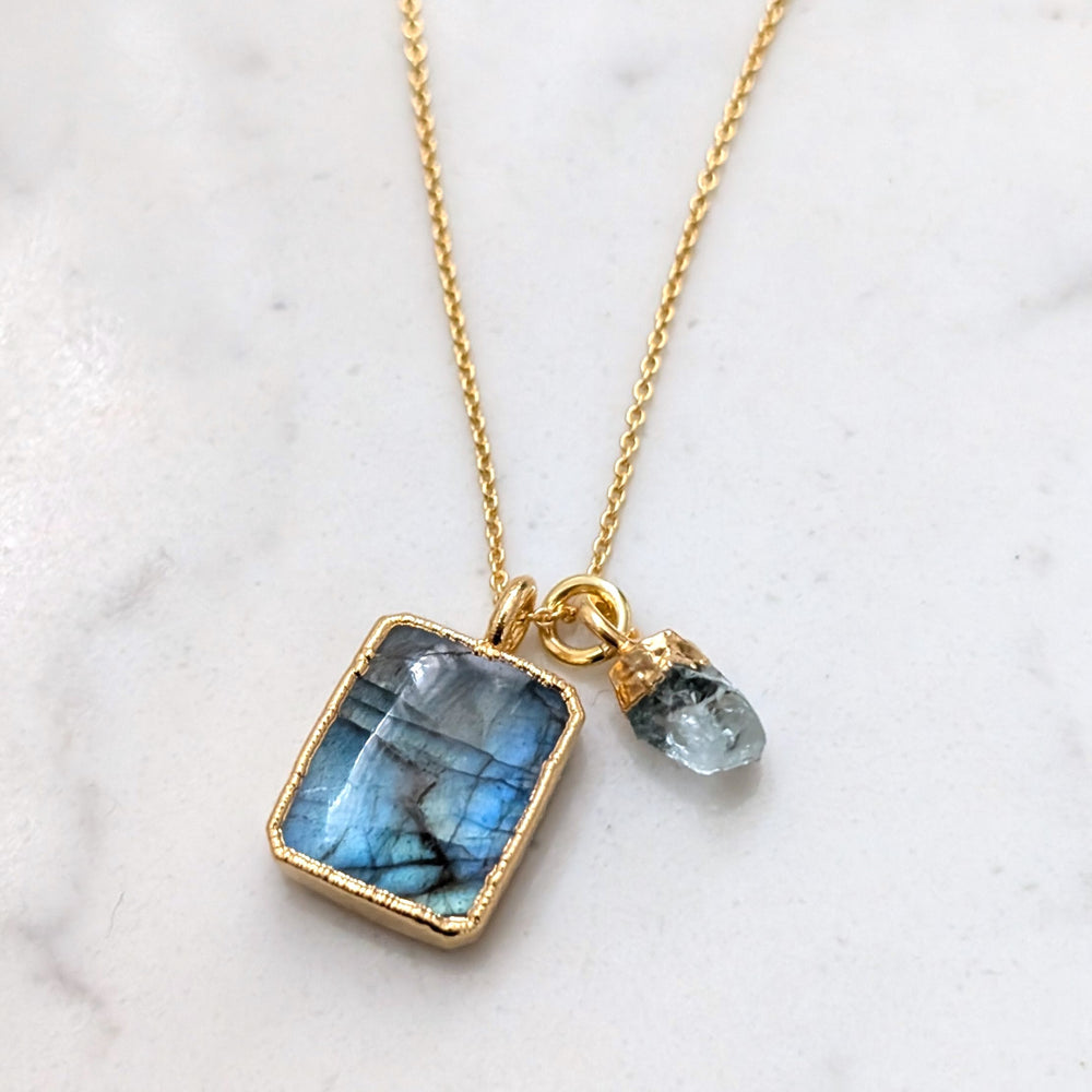 A gold-plated necklace featuring a rectangular labradorite pendant and a small aquamarine tumblestone charm.