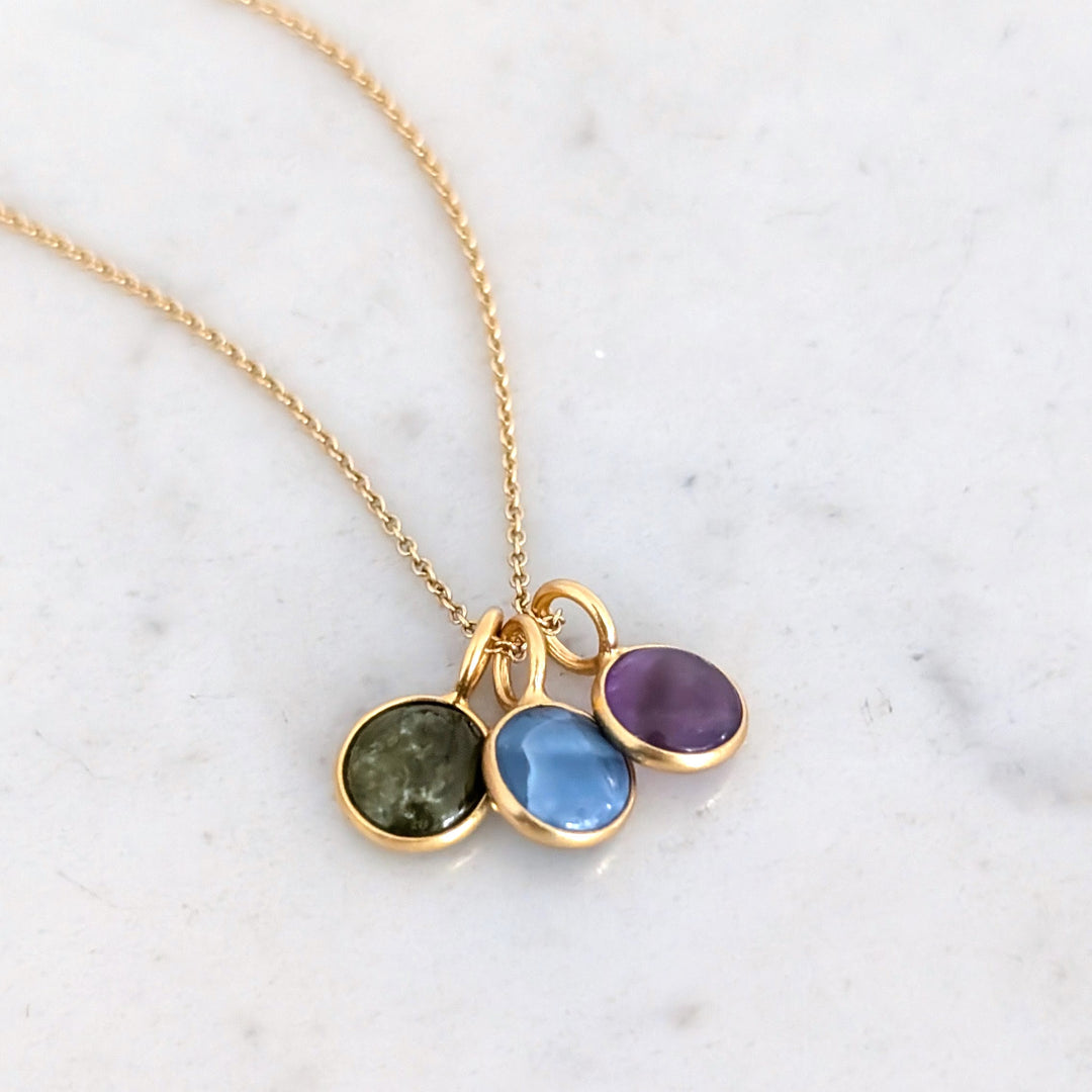 A birthstone necklace featuring multiple round gemstone charms in gold-colored settings on a gold cable chain.
