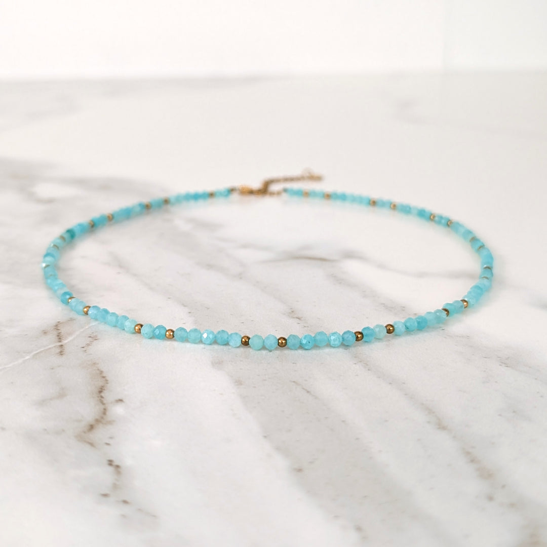 A delicate amazonite gemstone beaded necklace made of light blue faceted beads interspersed with gold beads.