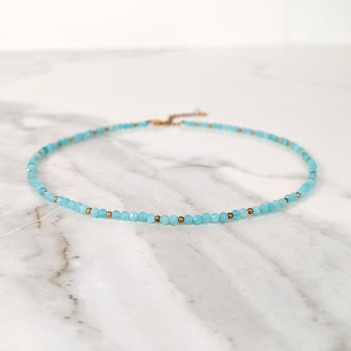A delicate amazonite gemstone beaded necklace made of light blue faceted beads interspersed with gold beads.