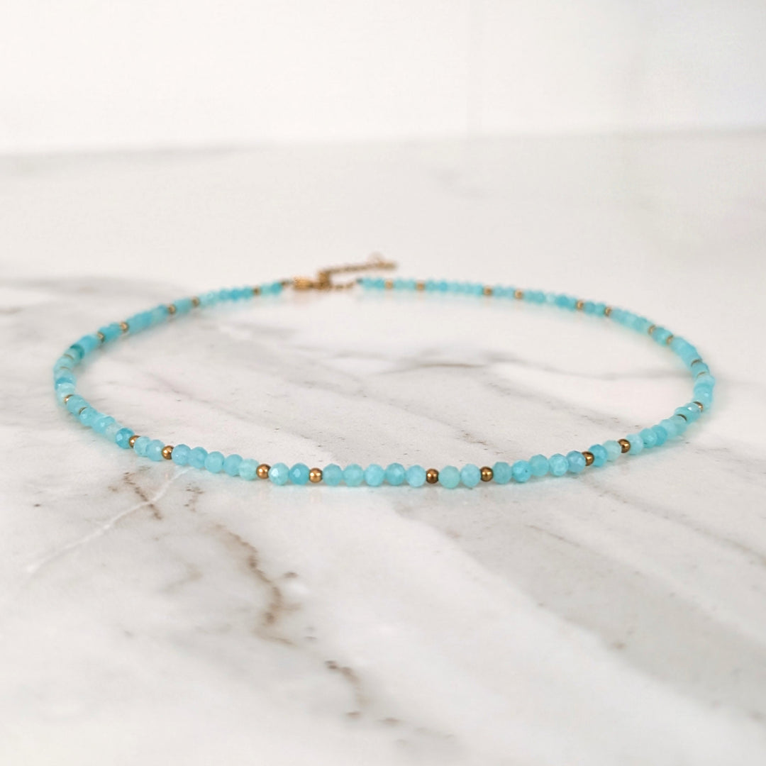 A delicate amazonite gemstone beaded necklace made of light blue faceted beads interspersed with gold beads.