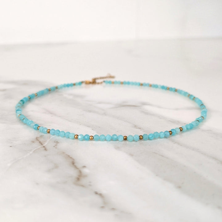 A delicate amazonite gemstone beaded necklace made of light blue faceted beads interspersed with gold beads.