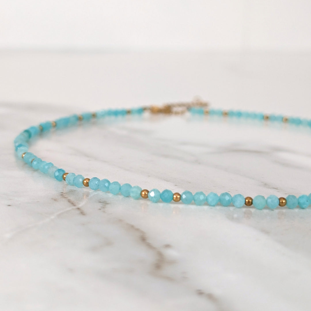 A delicate amazonite gemstone beaded necklace made of light blue faceted beads interspersed with gold beads.