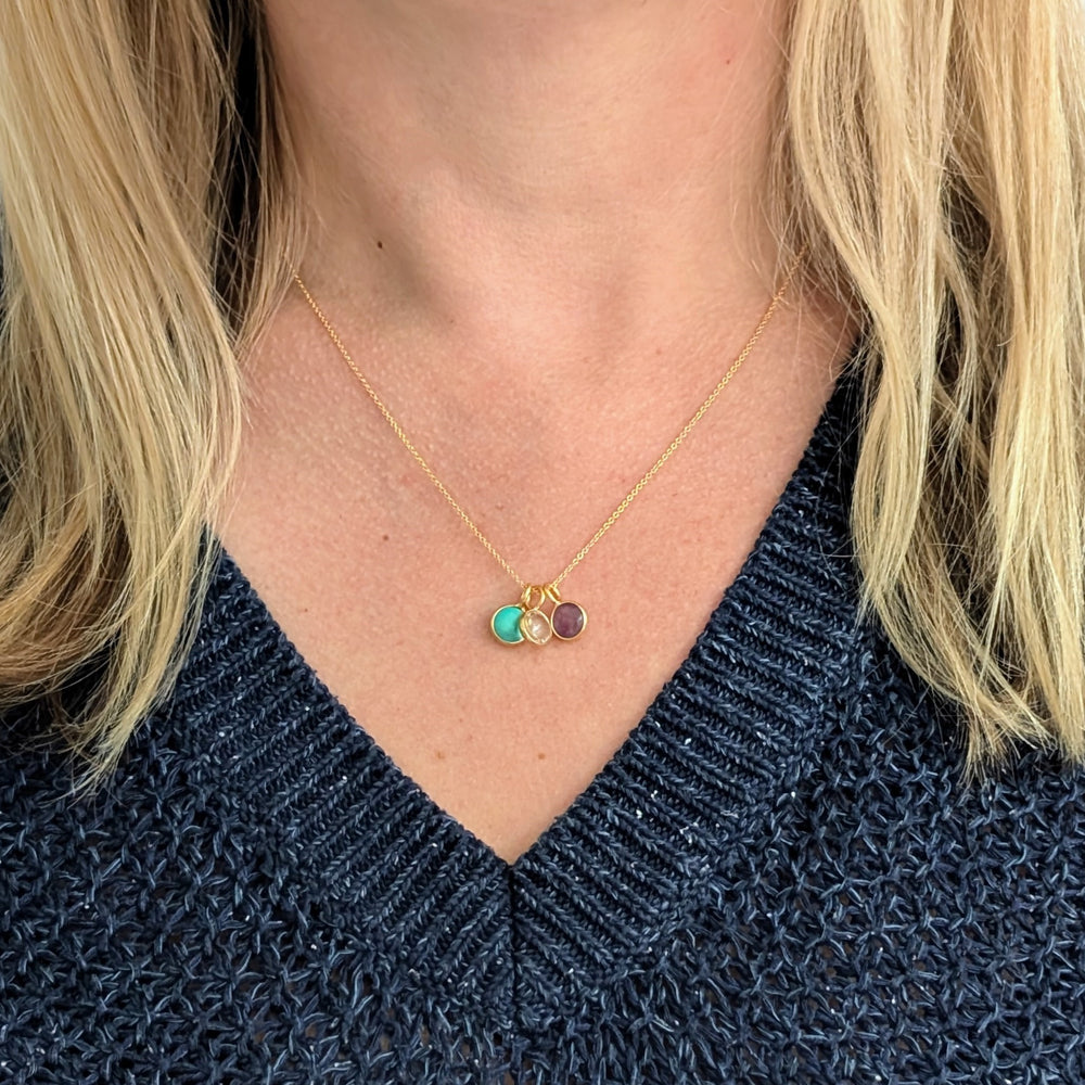 A birthstone necklace featuring multiple round gemstone charms in gold-colored settings on a gold cable chain.