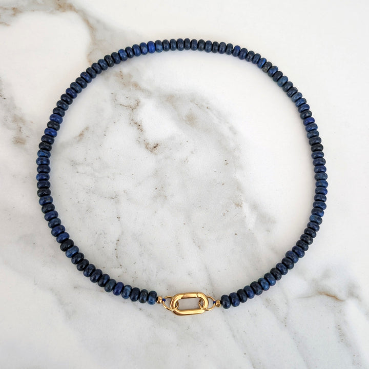 A gemstone beaded necklace made of blue lapis lazuli stones with a gold clasp.