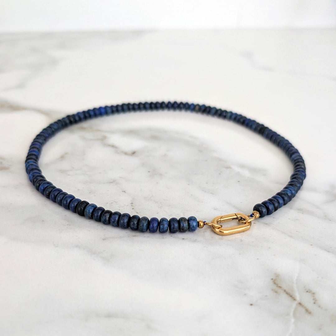 A gemstone beaded necklace made of blue lapis lazuli stones with a gold clasp.