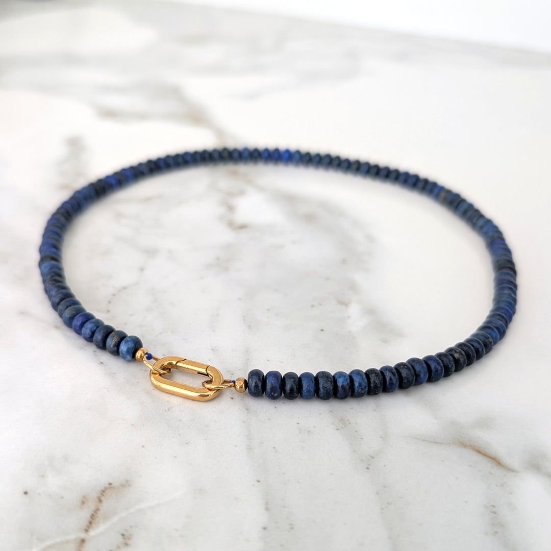 A gemstone beaded necklace made of blue lapis lazuli stones with a gold clasp.