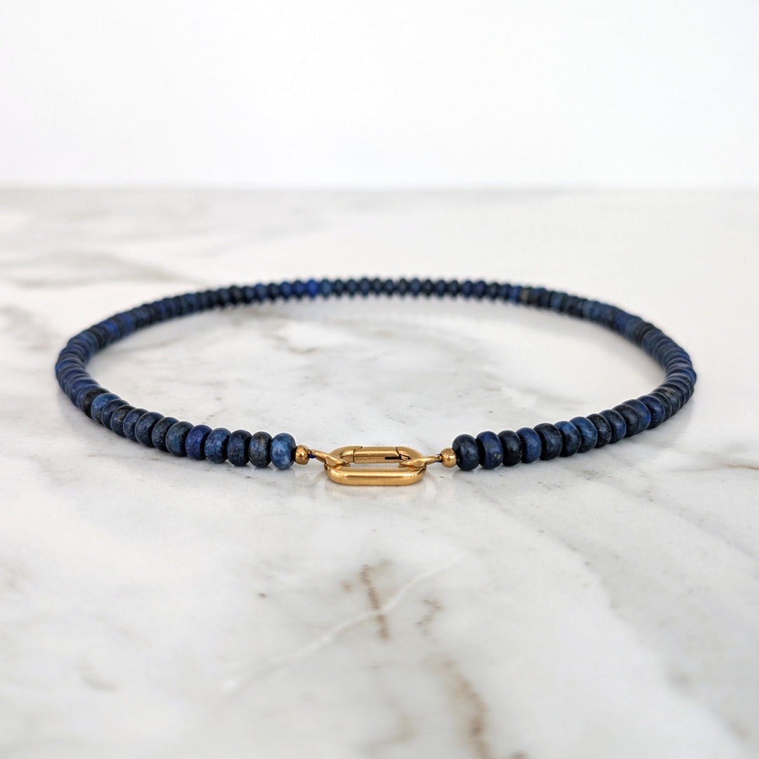 A gemstone beaded necklace made of blue lapis lazuli stones with a gold clasp.
