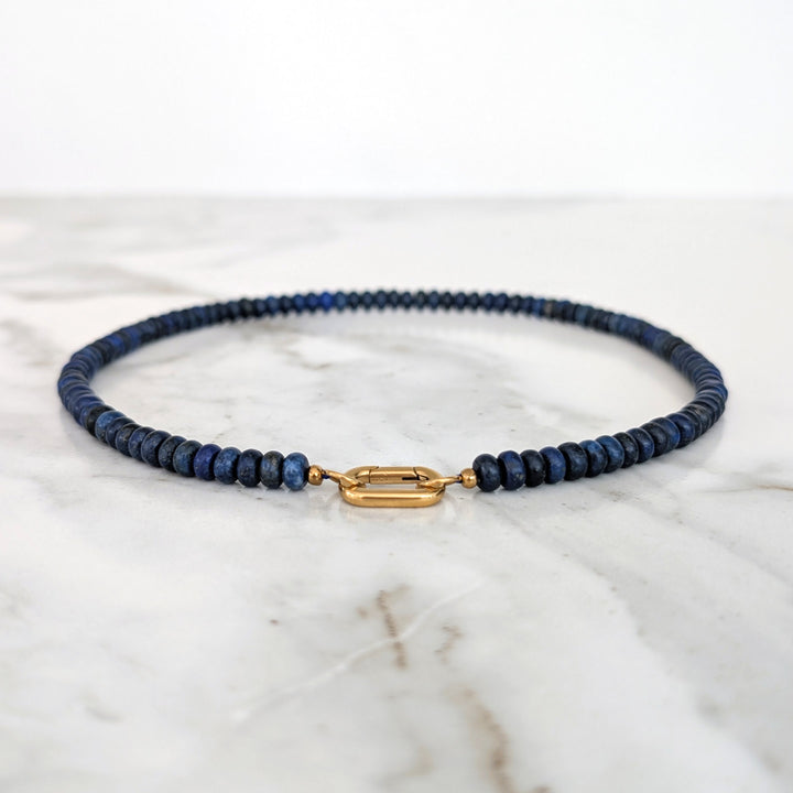 A gemstone beaded necklace made of blue lapis lazuli stones with a gold clasp.