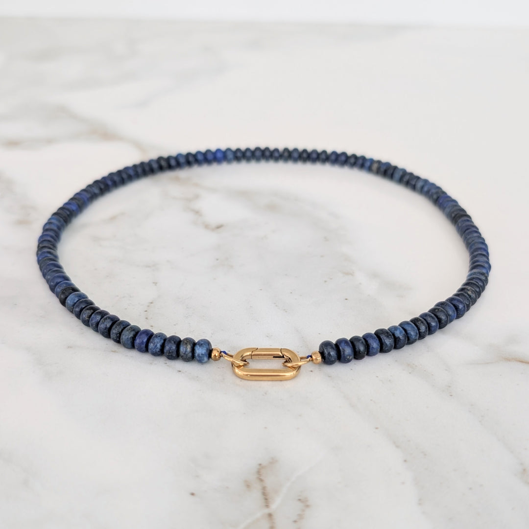 A gemstone beaded necklace made of blue lapis lazuli stones with a gold clasp.