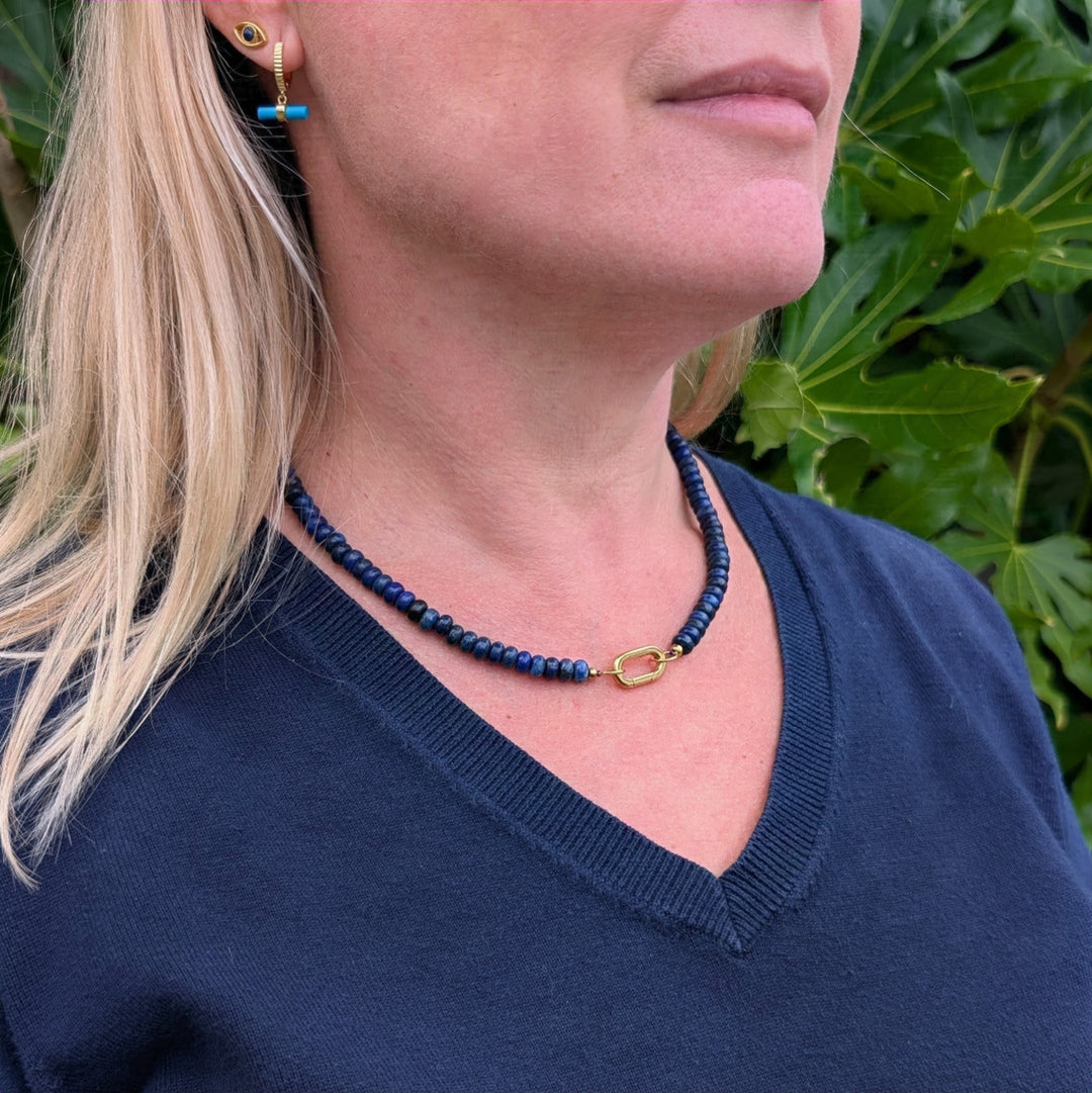 A gemstone beaded necklace made of blue lapis lazuli stones with a gold clasp.