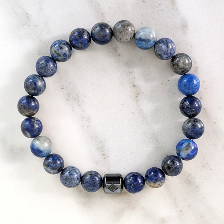 A beaded men's gemstone stretch bracelet made of polished blue and gray stone lapis lazuli beads and a hematite Lapis London logo bead.