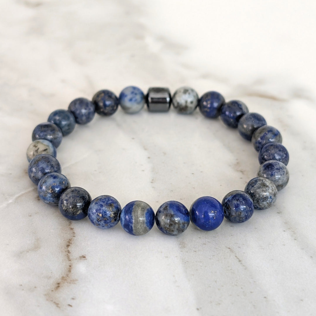 A beaded men's gemstone stretch bracelet made of polished blue and gray stone lapis lazuli beads and a hematite Lapis London logo bead.