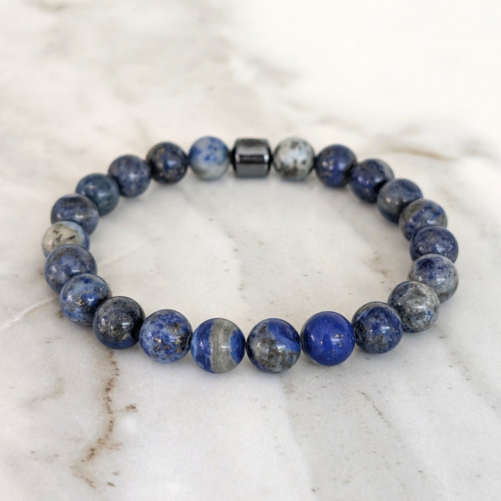 A beaded men's gemstone stretch bracelet made of polished blue and gray stone lapis lazuli beads and a hematite Lapis London logo bead.