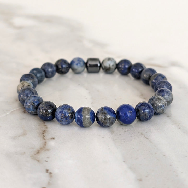 A beaded men's gemstone stretch bracelet made of polished blue and gray stone lapis lazuli beads and a hematite Lapis London logo bead.