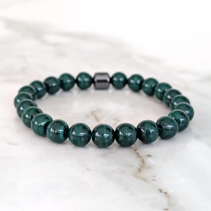 A men's 8mm beaded stretch bracelet made of polished dark green malachite beads with a single dark metallic hematite bead.