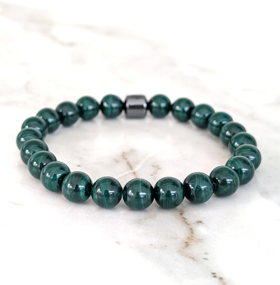 A men's 8mm beaded stretch bracelet made of polished dark green malachite beads with a single dark metallic hematite bead.