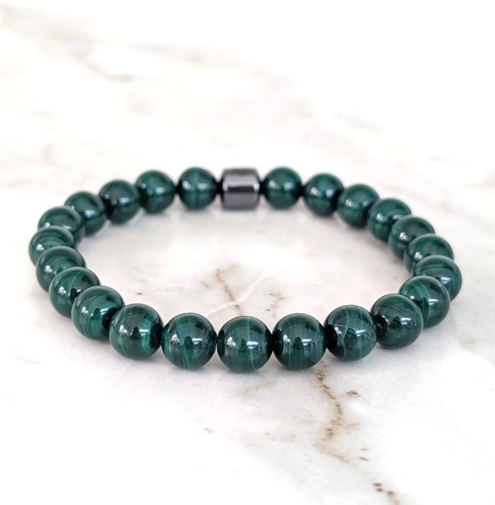 A men's 8mm beaded stretch bracelet made of polished dark green malachite beads with a single dark metallic hematite bead.
