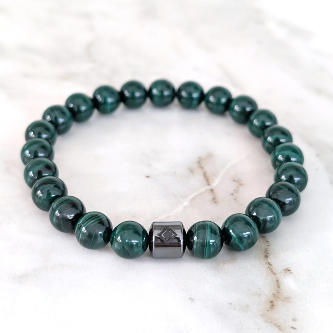 A men's 8mm beaded stretch bracelet made of polished dark green malachite beads with a single dark metallic hematite bead.