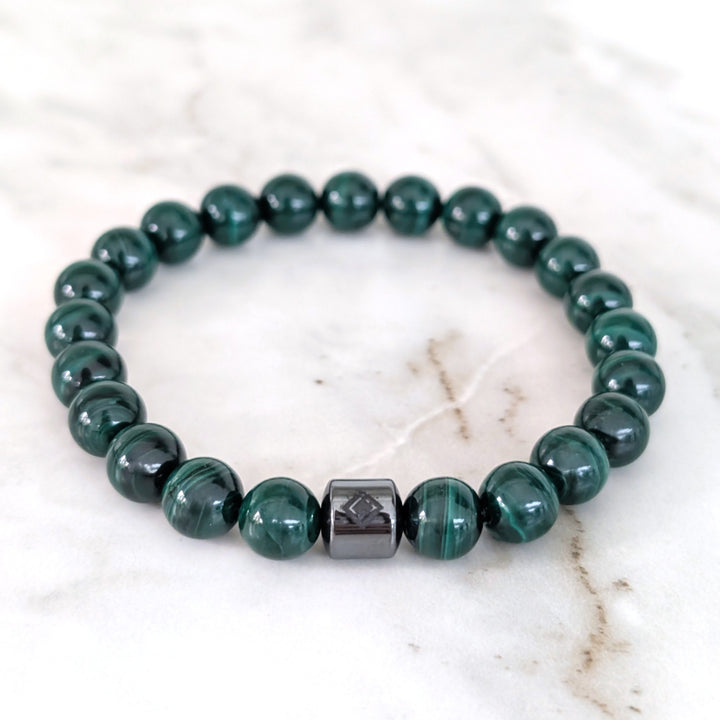 A men's 8mm beaded stretch bracelet made of polished dark green malachite beads with a single dark metallic hematite bead.
