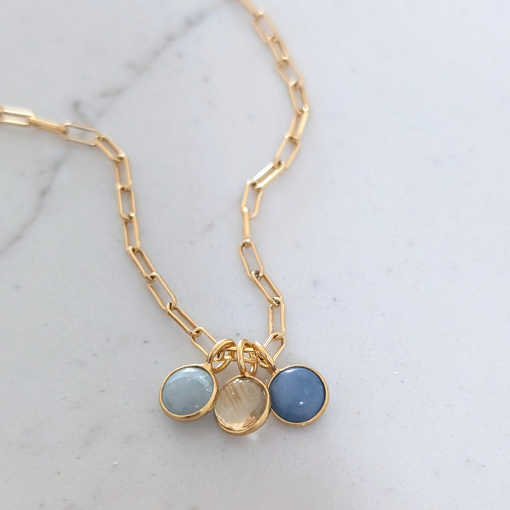 A birthstone necklace featuring multiple round gemstone charms in gold-colored settings on a gold cable chain.