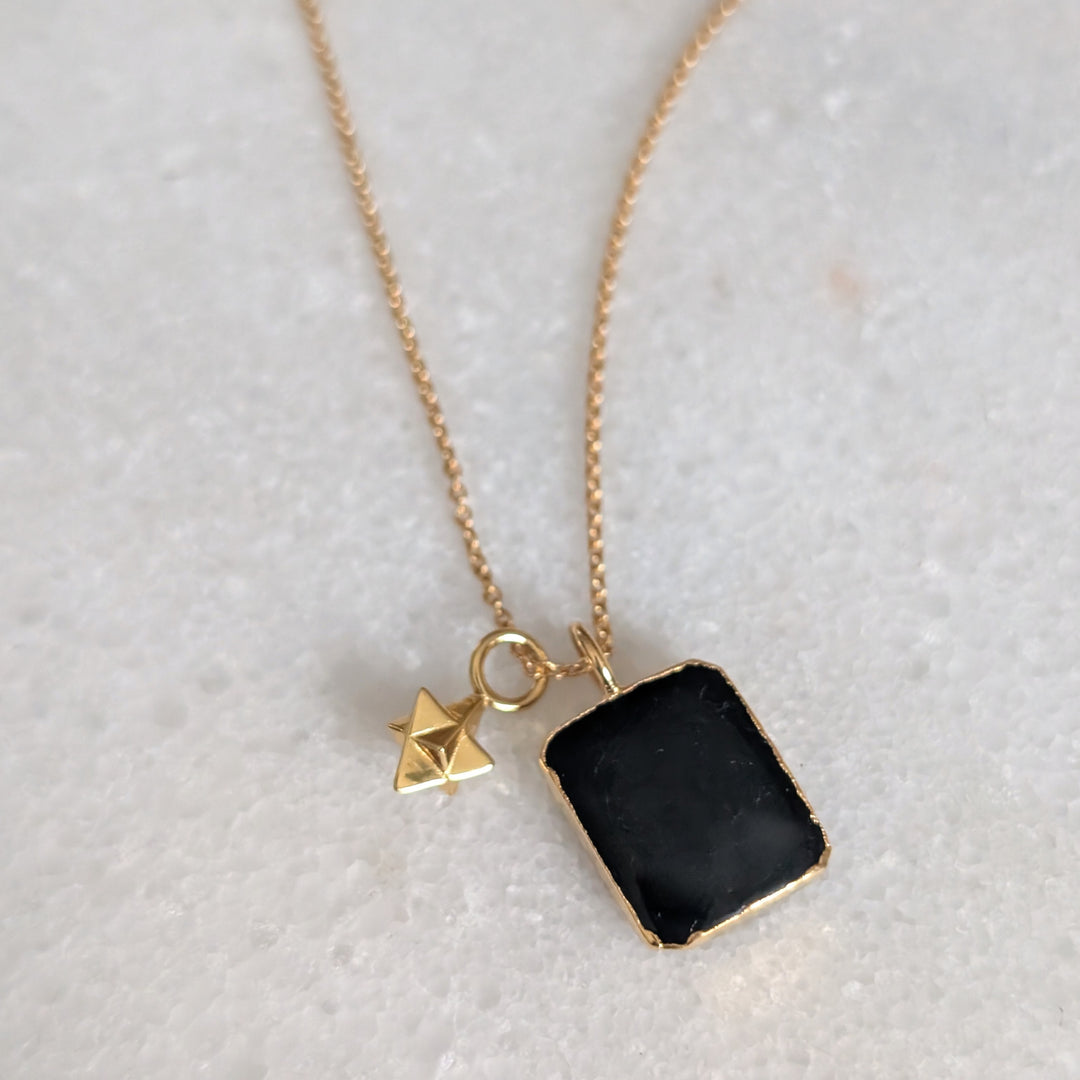 Necklace with a black tourmaline rectangular pendant and gold chain on a light gray background