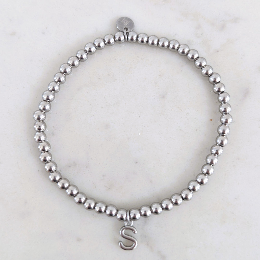 A silver stainless steel PVD beaded stretch bracelet with alphabet letter charm.