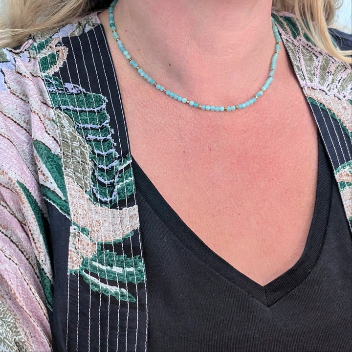 A delicate amazonite gemstone beaded necklace made of light blue faceted beads interspersed with gold beads.