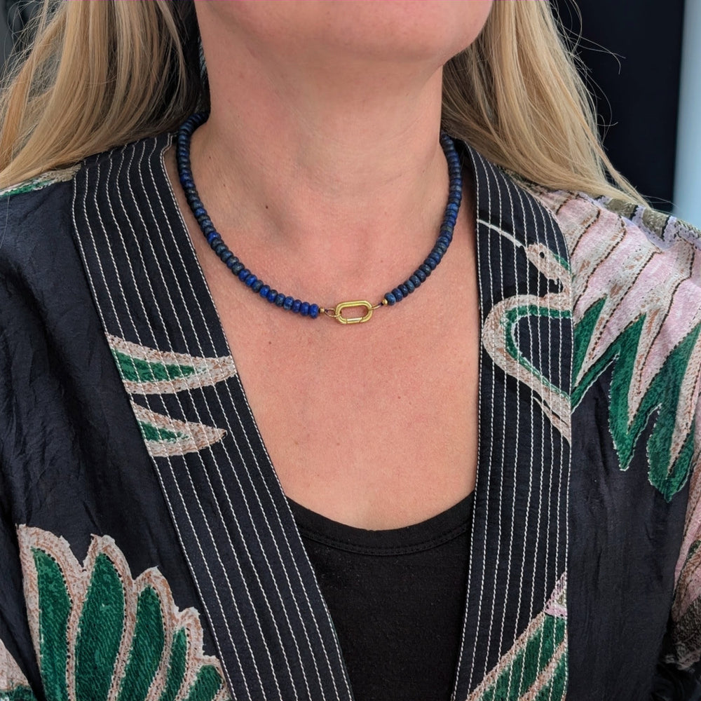 A gemstone beaded necklace made of blue lapis lazuli stones with a gold clasp.