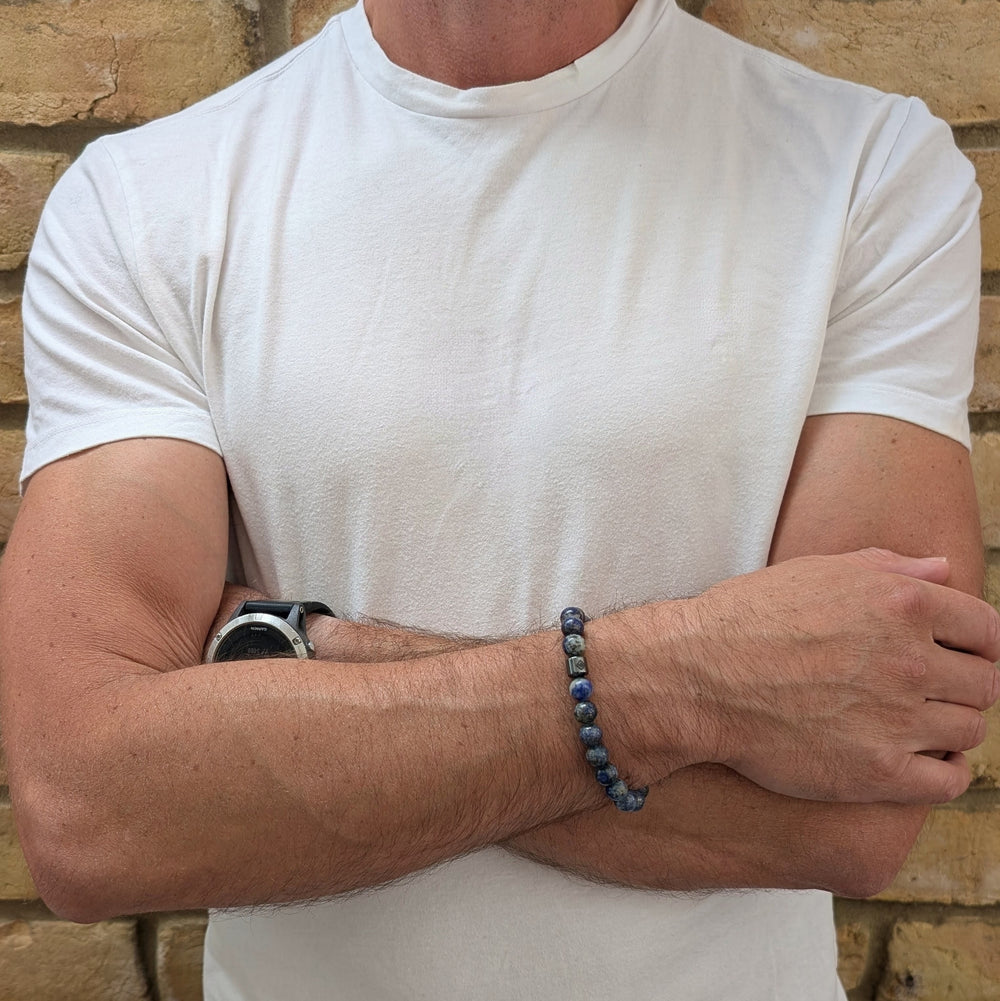 A beaded men's gemstone stretch bracelet made of polished blue and gray stone lapis lazuli beads and a hematite Lapis London logo bead.