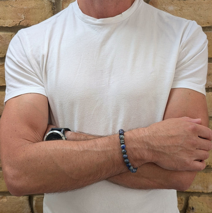 A beaded men's gemstone stretch bracelet made of polished blue and gray stone lapis lazuli beads and a hematite Lapis London logo bead.