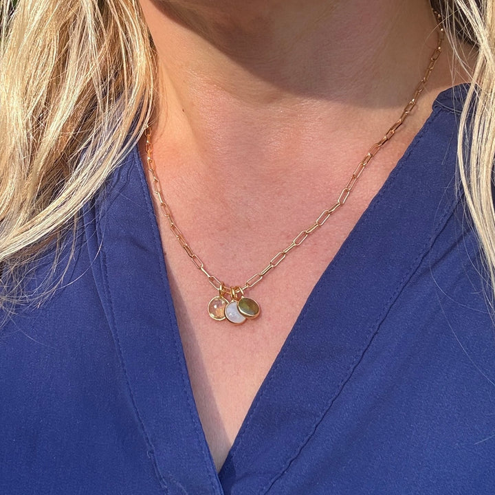 A birthstone necklace featuring multiple round gemstone charms in gold-colored settings on a gold cable chain.
