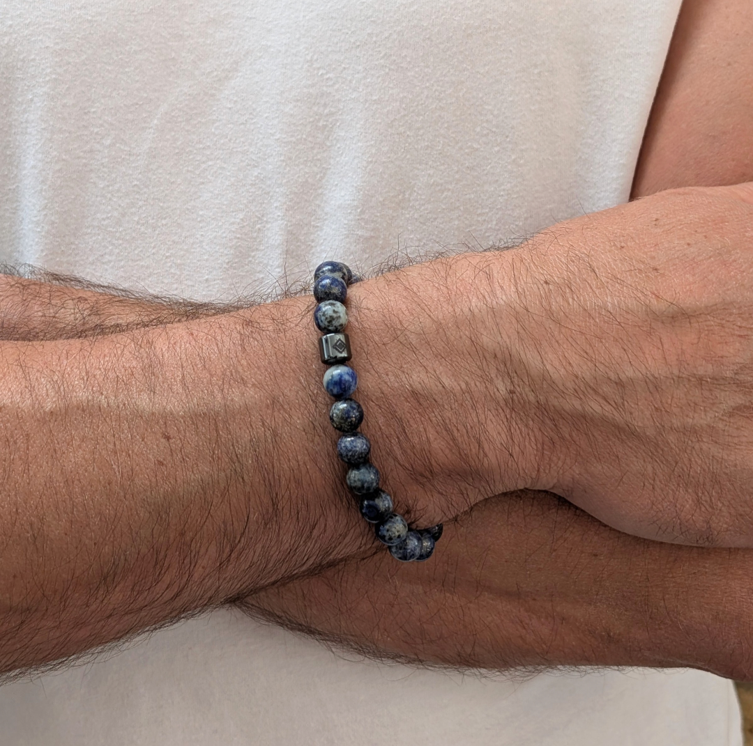 A beaded men's gemstone stretch bracelet made of polished blue and gray stone lapis lazuli beads and a hematite Lapis London logo bead.
