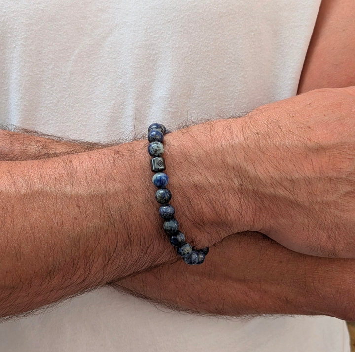 A beaded men's gemstone stretch bracelet made of polished blue and gray stone lapis lazuli beads and a hematite Lapis London logo bead.